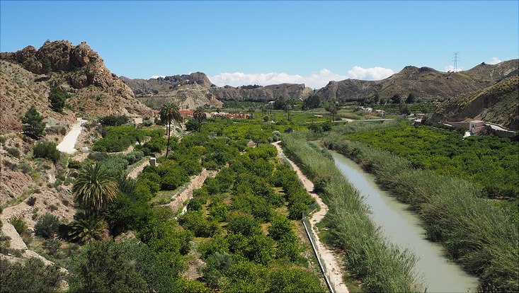 Fluss durchläuft ein Tal, am Ufer sind Terrassenfelder zu erkennen, Hügel umschließen die Szene, blauer Himmel, mediterrane Vegetation