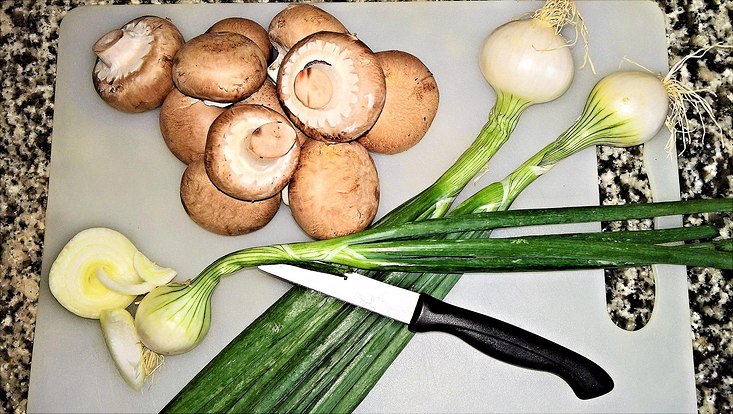 Lauchzwiebeln und Champignons auf einem Schweidebrett mit einem Messer daneben / Spring onions and Champignons on a cutting board