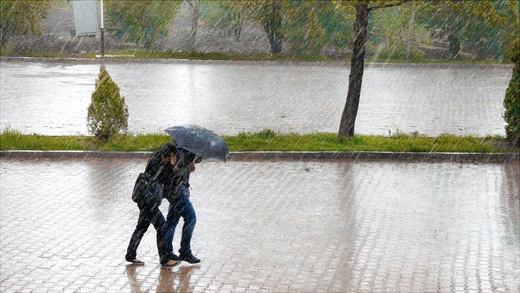 Zwei Personen gehen unter einem Regenschirm geduckt über eine Straße während starker Regen fällt