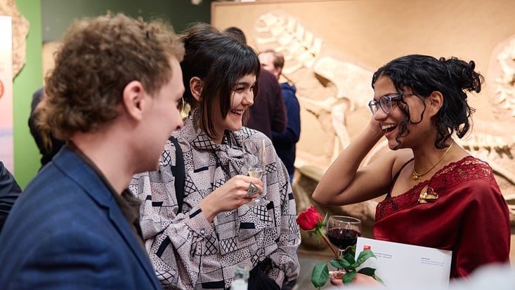 Drei Absolvent:innen sprechen lachend miteinander, im Hintergrund sieht man Fossilien.