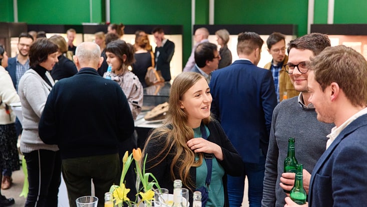 Teilnehmende der Feierlichkeiten stehen um Stehtische herum und sprechen miteinander.